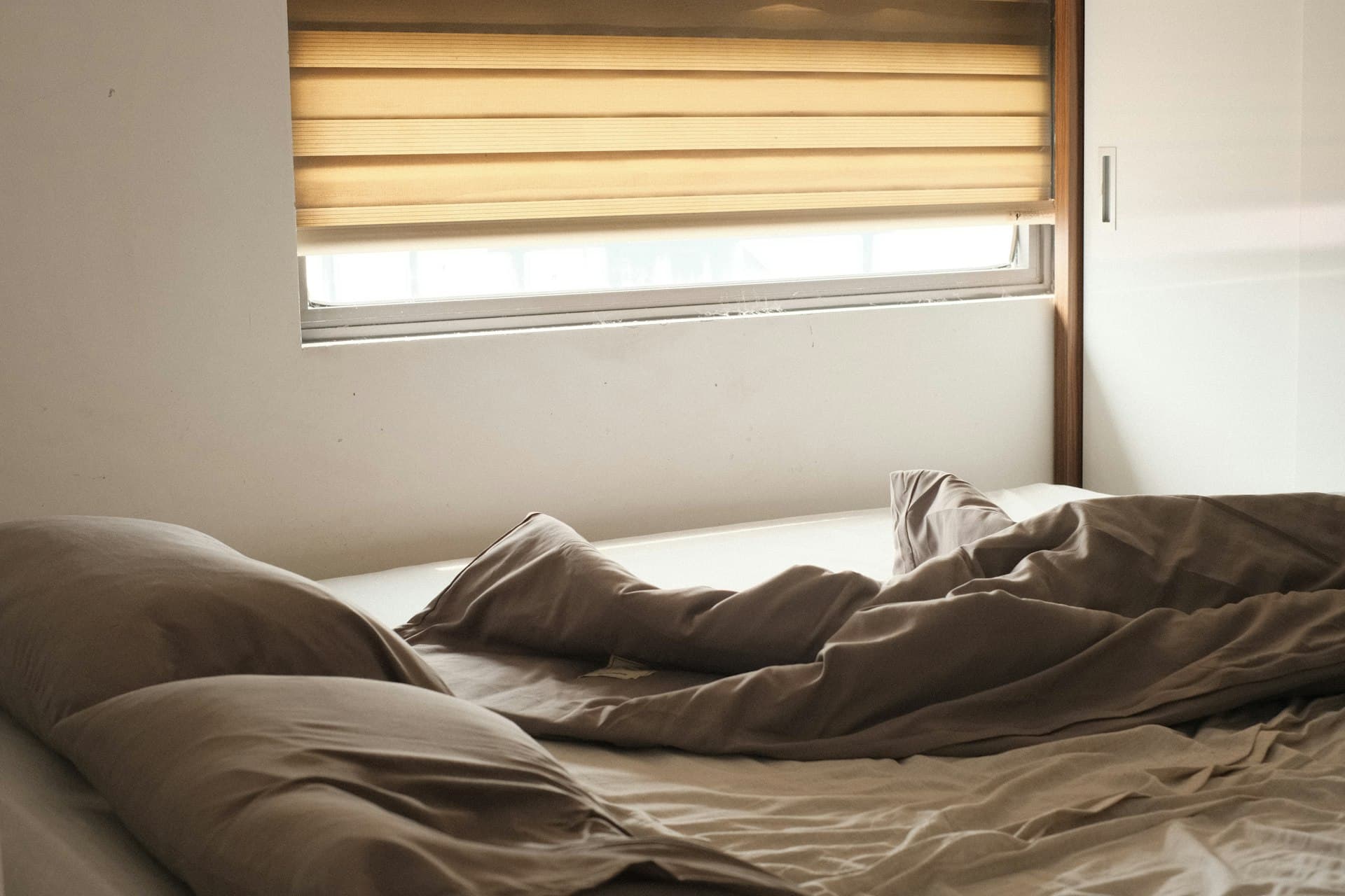 Warm Roman fold blind glowing over a bed at dusk
